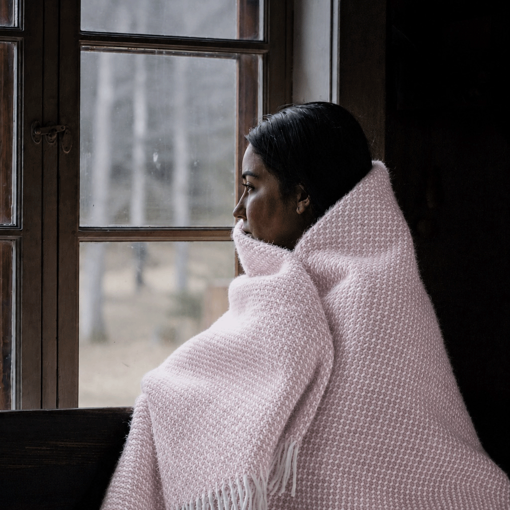 Girl at a window wrapped in Preppy pale pink lambswool throw from Klippan