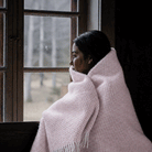 Girl at a window wrapped in Preppy pale pink lambswool throw from Klippan