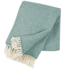 A mint green lambswool throw with a geometric pattern and a fringe, displayed on a neutral background.